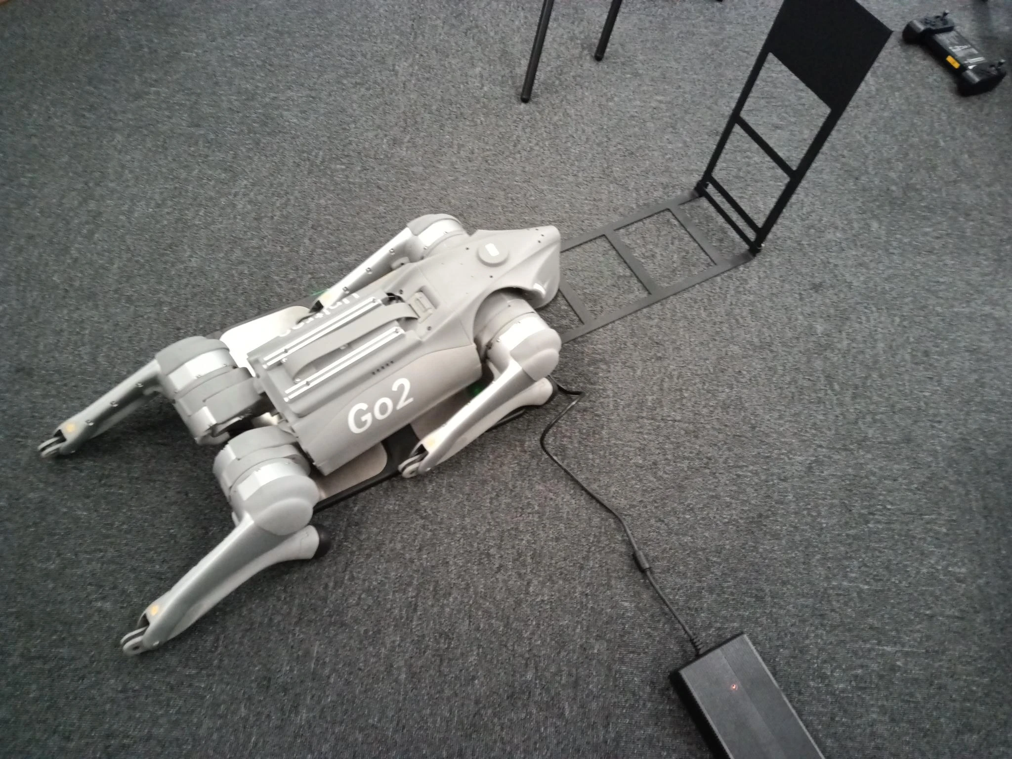 Unitree Go2 self-charging board in use with a Go2 EDU robot lying on the pad, belly charging contacts pressed against the board in a lab environment
